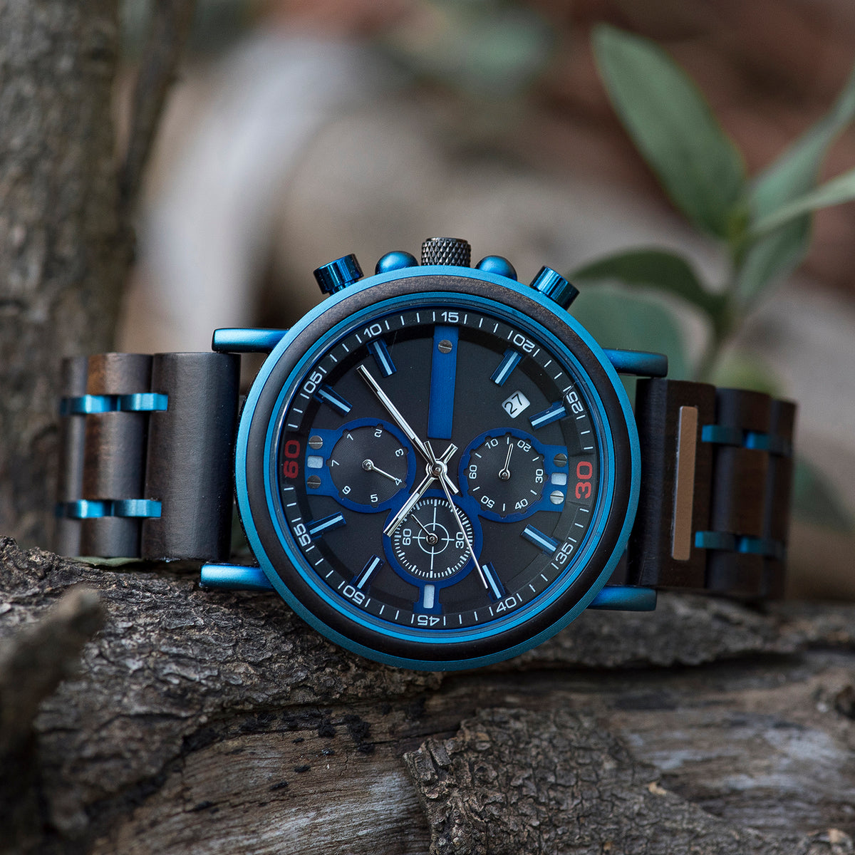 A stylish men's chronograph watch featuring blue metallic accents, a dark dial with multiple sub-dials, and a mixed-material band, presented on a rustic wood background to highlight its sporty and sophisticated design.
