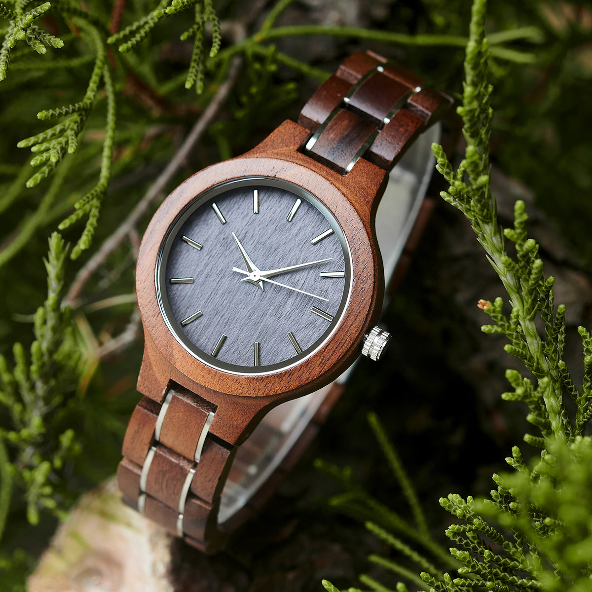 A stylish women's walnut watch with silver-tone accents, showcased amidst lush greenery to highlight its natural wood grain and elegant design.