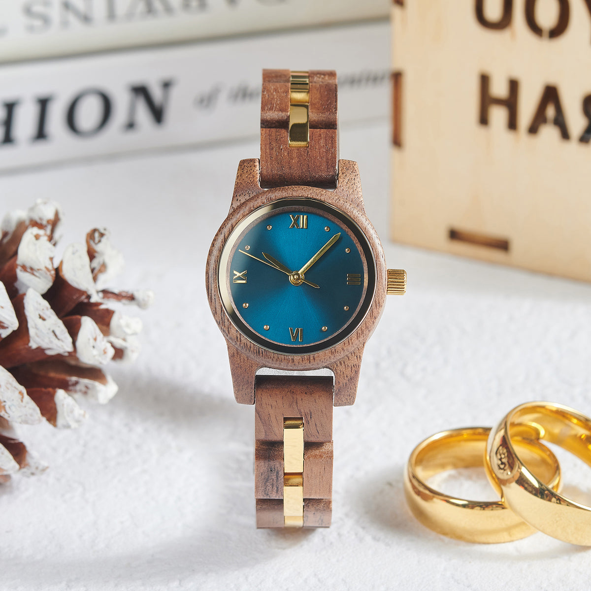 A stylish women's wooden watch with a blue dial and gold accents, presented with vintage elements like a pinecone and gold rings to highlight its elegant and timeless aesthetic.