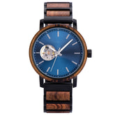 Front view of a wristwatch with a blue dial, skeleton movement window, and a band combining wood and black metal, isolated on a white background.