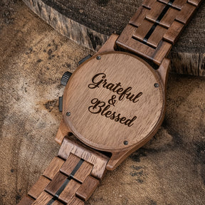 The back of a men's watch with a brown wooden case and band, featuring metal accents, placed on a textured, earthy-toned surface with rustic wood elements in the background.