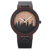 A unique dark wooden watch featuring a runic symbol bezel, forest silhouette dial, black leather band, and gold-tone hands, displayed against a white background.