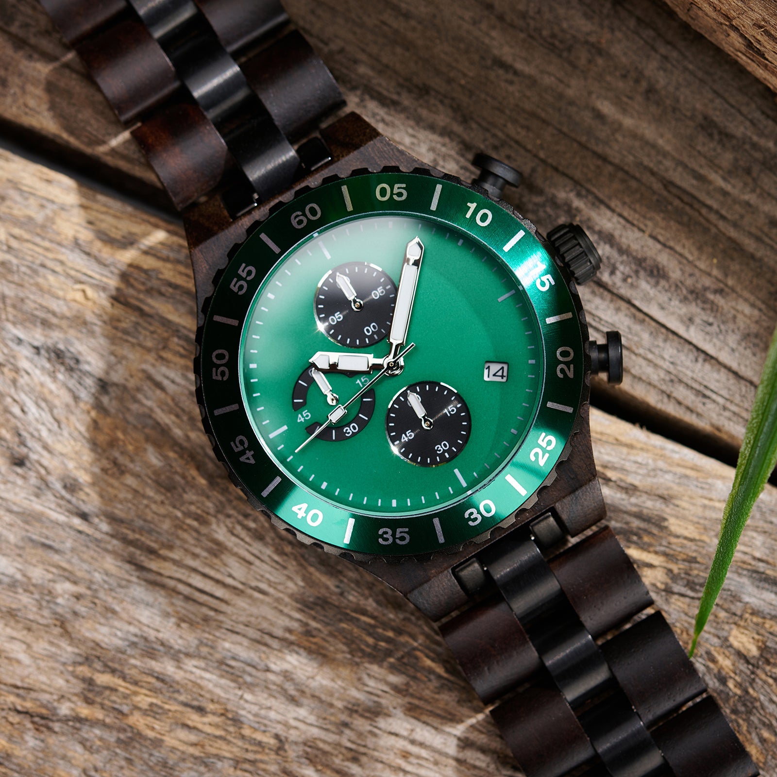 A detailed view of a men's dark wooden chronograph watch with green accents, displayed on a wooden surface to emphasize its craftsmanship and sophisticated design.