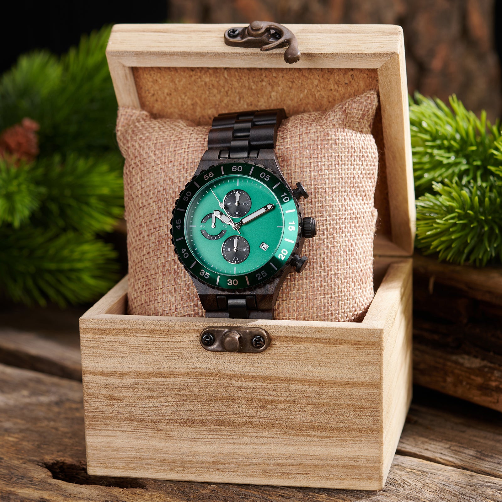 A sophisticated men's dark wooden chronograph watch with green accents, presented in a wooden box with a burlap cushion, set against a backdrop of lush greenery to emphasize its natural and refined packaging.