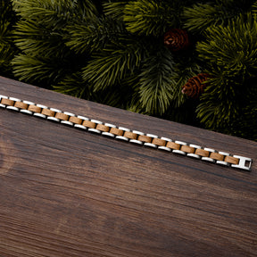 Men's wooden bracelet with stainless steel links on wood surface, surrounded by pine foliage. Rustic modern design, perfect for stylish, nature-loving men.