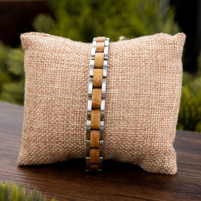 Men's wooden bracelet with stainless steel links on burlap pillow, nature background. Rustic modern design, ideal for stylish, outdoorsy men seeking unique accessories.