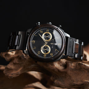 A stylish men's wooden chronograph watch with a black dial and gold accents, showcased on natural wood to highlight its sophisticated and rugged design.