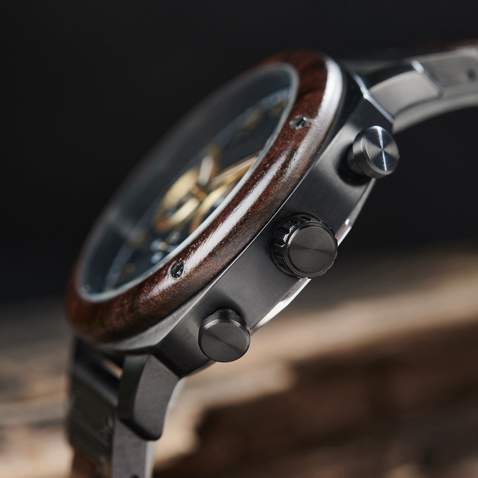 A detailed side view of a men's wooden chronograph watch with a black dial and gold accents, emphasizing the craftsmanship of its wooden bezel and metallic components.