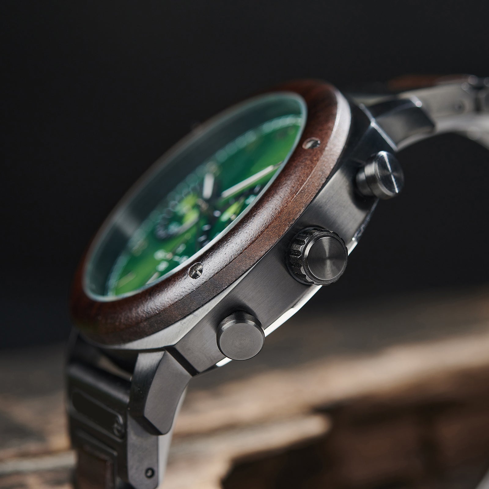 A detailed side view of a men's wooden chronograph watch with a green dial, emphasizing the craftsmanship of its wooden bezel and metallic accents.