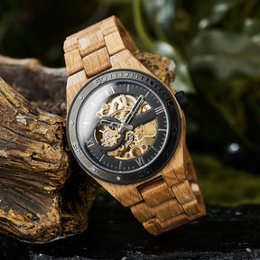 A men's automatic mechanical watch featuring an oak wood strap and black stainless steel elements, showcasing a skeleton dial with visible golden gears, positioned on textured wood against a natural, green-inspired background.