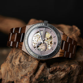 A men's automatic mechanical watch crafted from walnut wood and black stainless steel, featuring a skeleton dial that reveals intricate movement, placed on textured wood against a dark background.