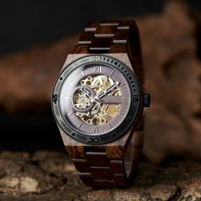 A men's automatic mechanical watch crafted from walnut wood and black stainless steel, featuring a skeleton dial that reveals intricate movement, placed on textured tree bark with a dark, natural background.
