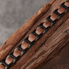 Close-up of men's bracelet with black stainless steel and walnut wood links, placed on natural wood, emphasizing its rugged and stylish design for men's fashion.