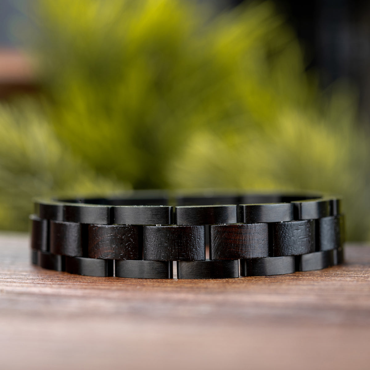 Men's black wooden link bracelet with sleek design, crafted from natural wood, a stylish and rugged accessory for men, displayed on wood with greenery background.
