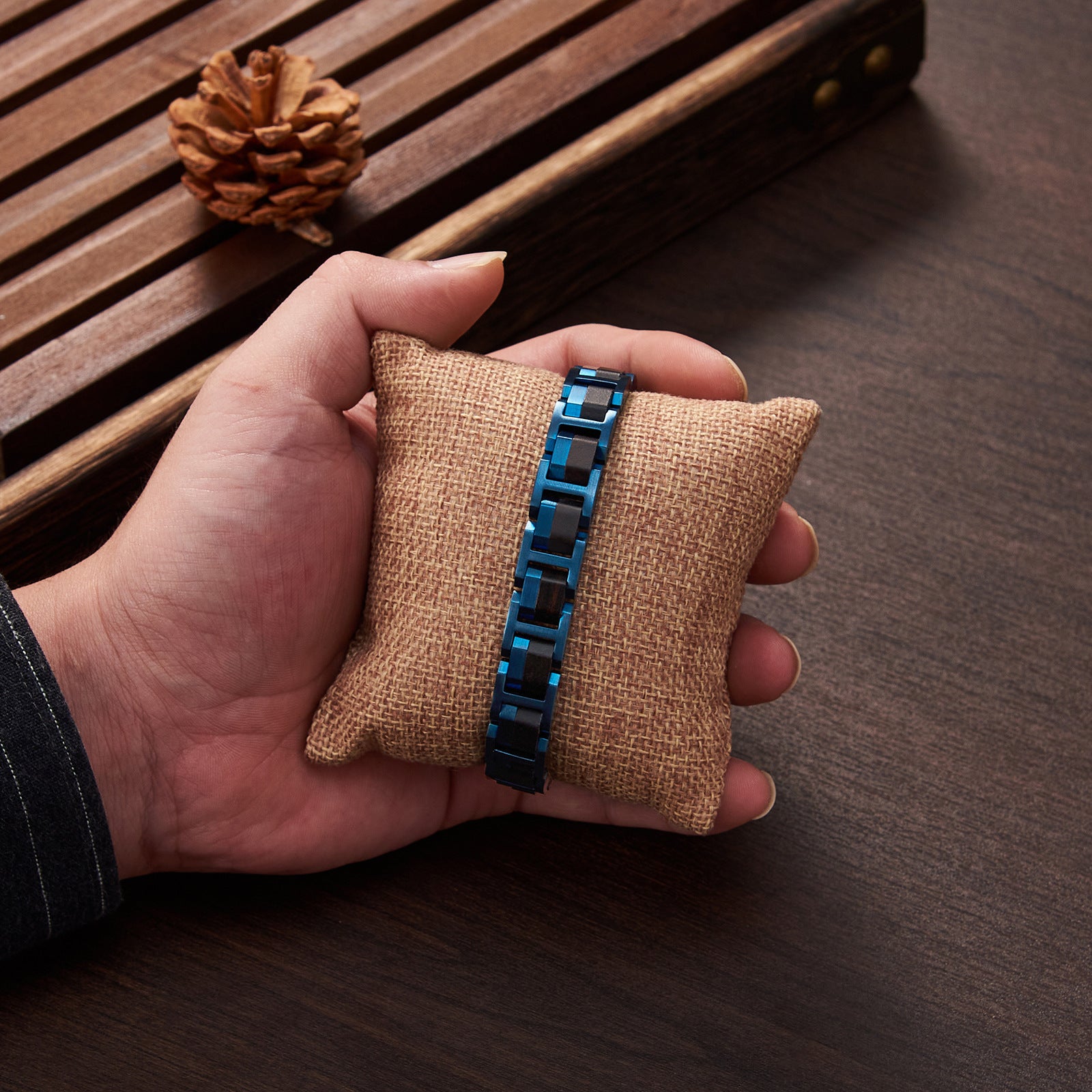 Men's bracelet made of blue stainless steel and ebony wood, displayed on a burlap pillow with rustic wooden background, a trendy wooden jewelry piece for men.