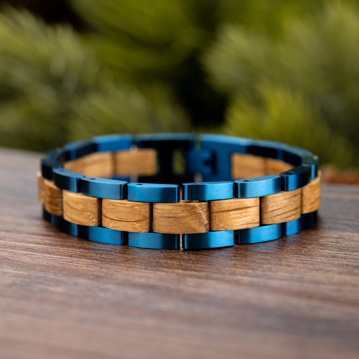 Men's wooden link bracelet with blue stainless steel accents, crafted from natural wood, a stylish and unique accessory for men, displayed on wood with greenery background.