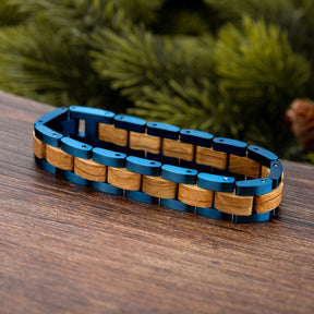 Men's trendy bracelet featuring blue stainless steel and natural oak wood links, showcased on a wooden surface with a rustic green background, ideal for men's fashion accessories.