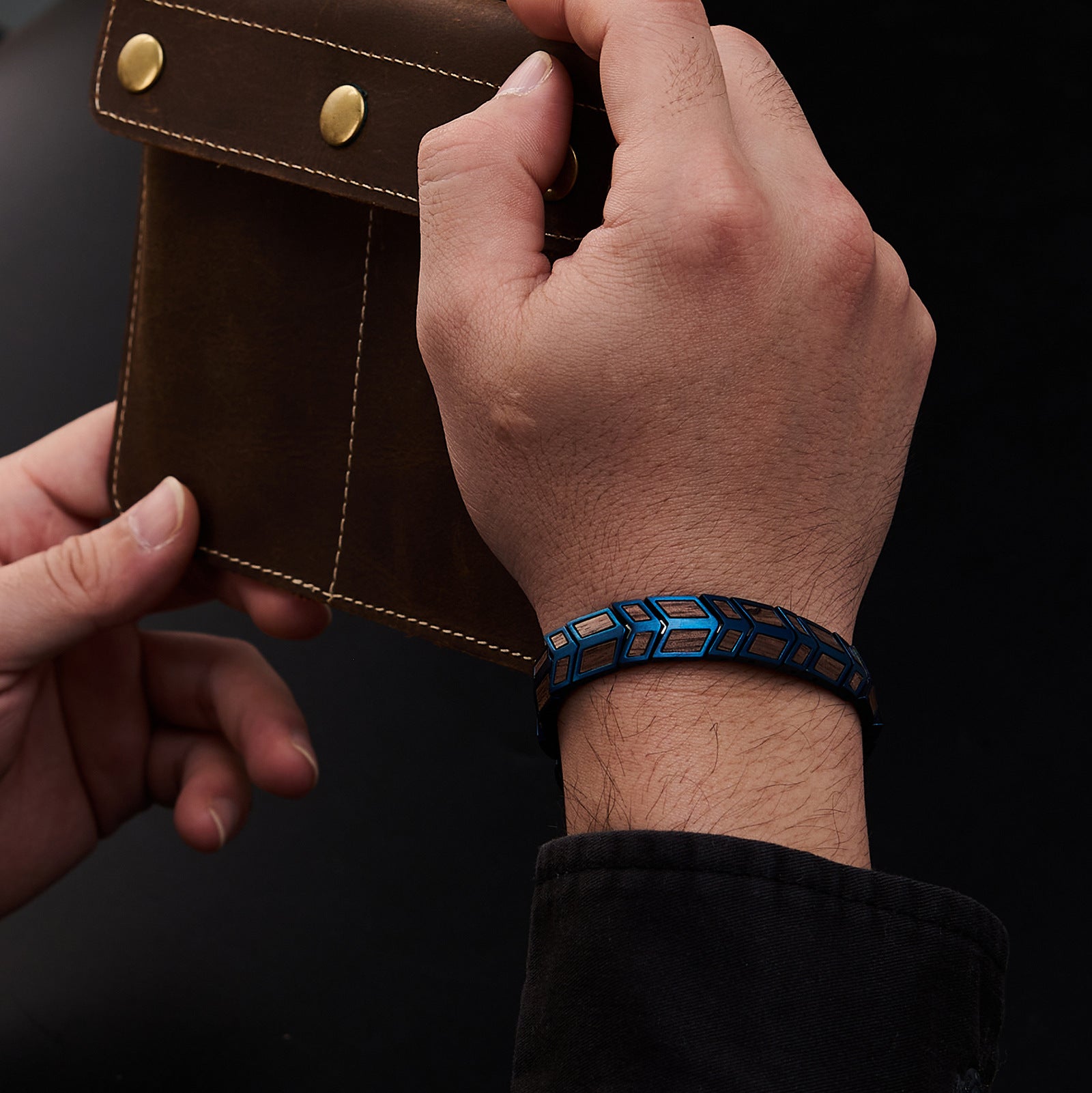 Men's hand wearing a blue stainless steel bracelet with walnut wood inlays, paired with a leather accessory. A fashionable, masculine jewelry piece for everyday style.