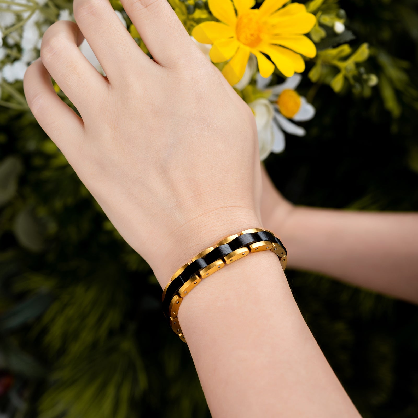 Men's black wooden link bracelet with gold-tone stainless steel, showcased on a wrist against a vibrant floral backdrop, a fashionable accessory for men.