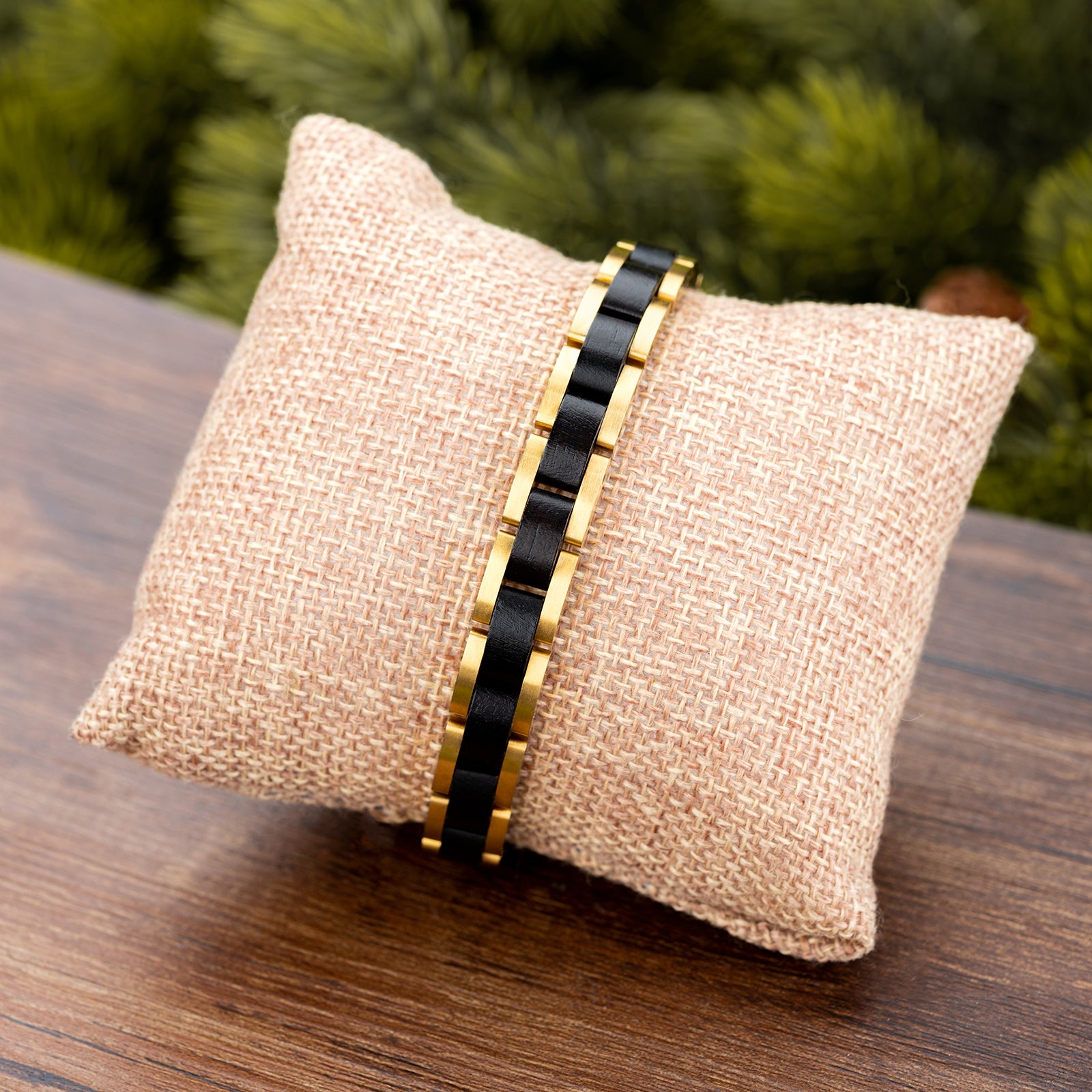 Men's black wooden link bracelet with gold-tone stainless steel, displayed on a burlap pillow with natural greenery, a stylish and unique men's accessory.