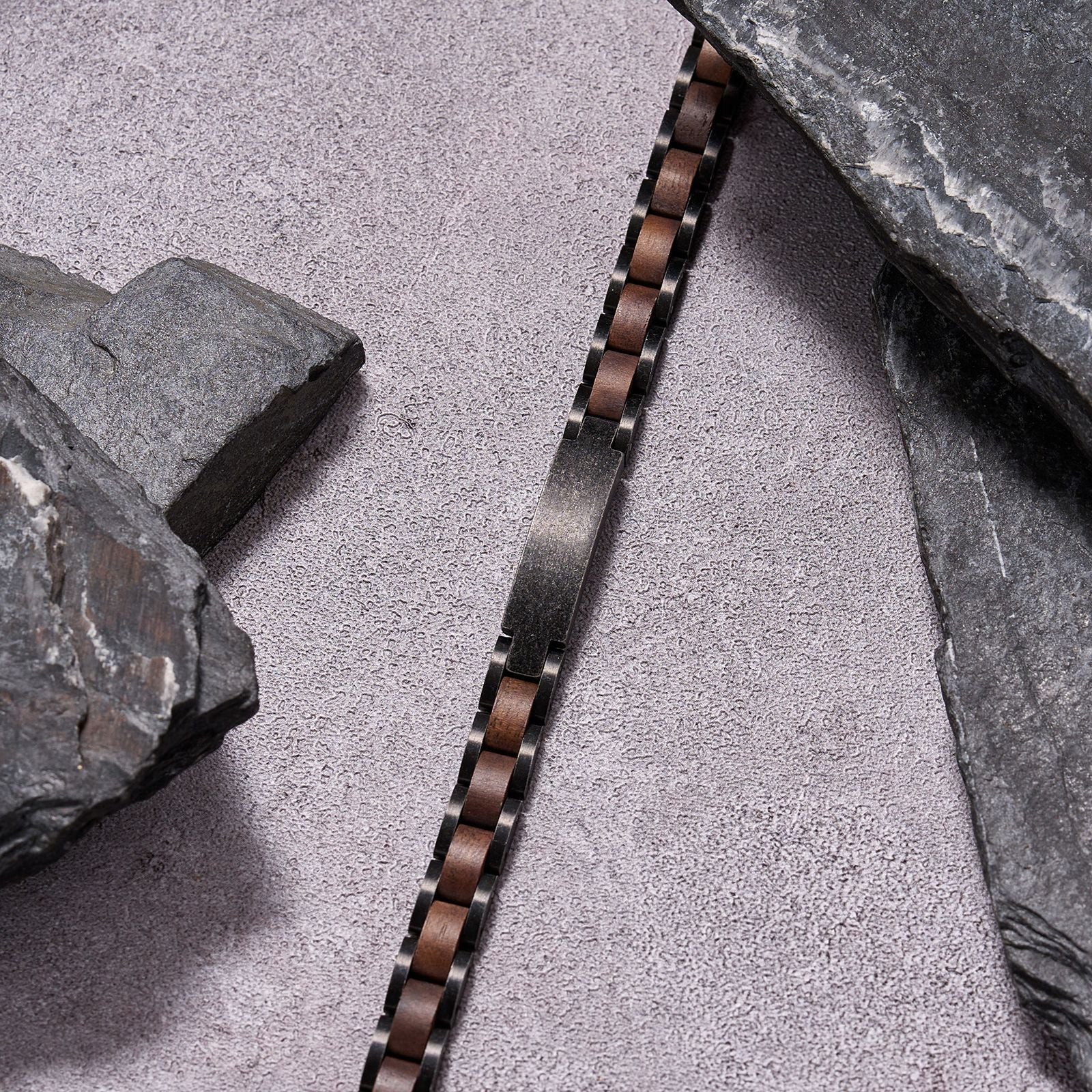 Men's bracelet made of gunmetal stainless steel and walnut wood, placed among stones for a rugged look, a stylish accessory perfect for men who love unique, durable jewelry.