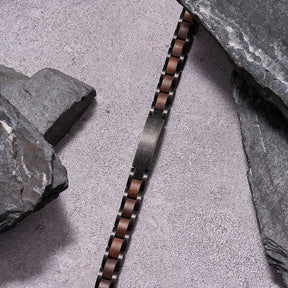 Men's bracelet made of gunmetal stainless steel and walnut wood, placed among stones for a rugged look, a stylish accessory perfect for men who love unique, durable jewelry.