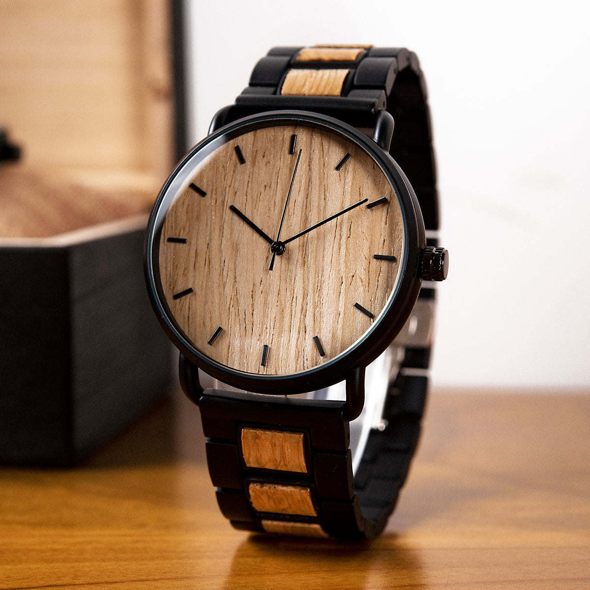 A minimalist men's watch featuring a natural wooden dial, black metal and wood accent band, presented on a wooden surface to highlight its sleek and natural design aesthetic.