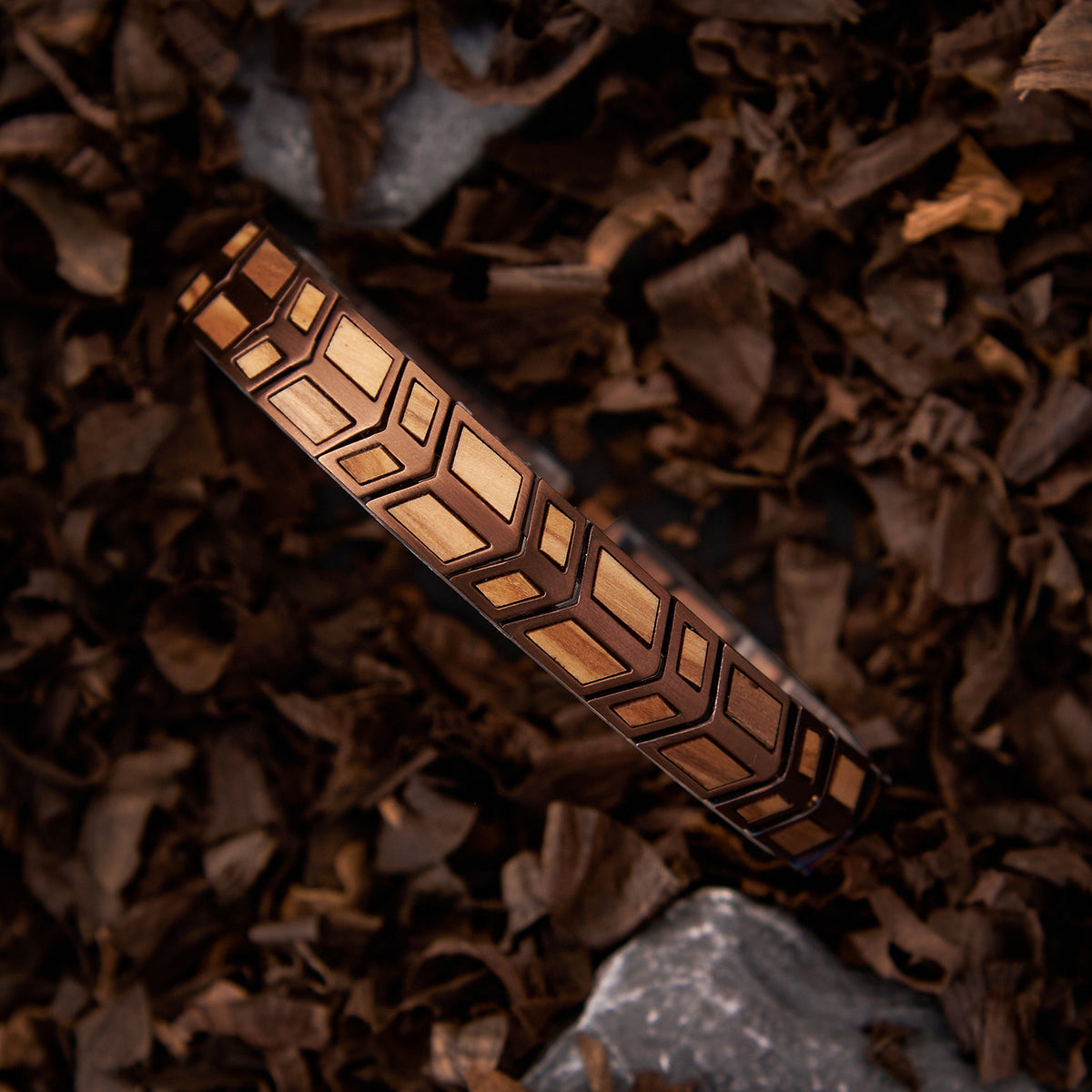 Men's bracelet with rose gold stainless steel and olive wood geometric design, placed on natural leaves and stones. A unique, fashionable accessory for men.