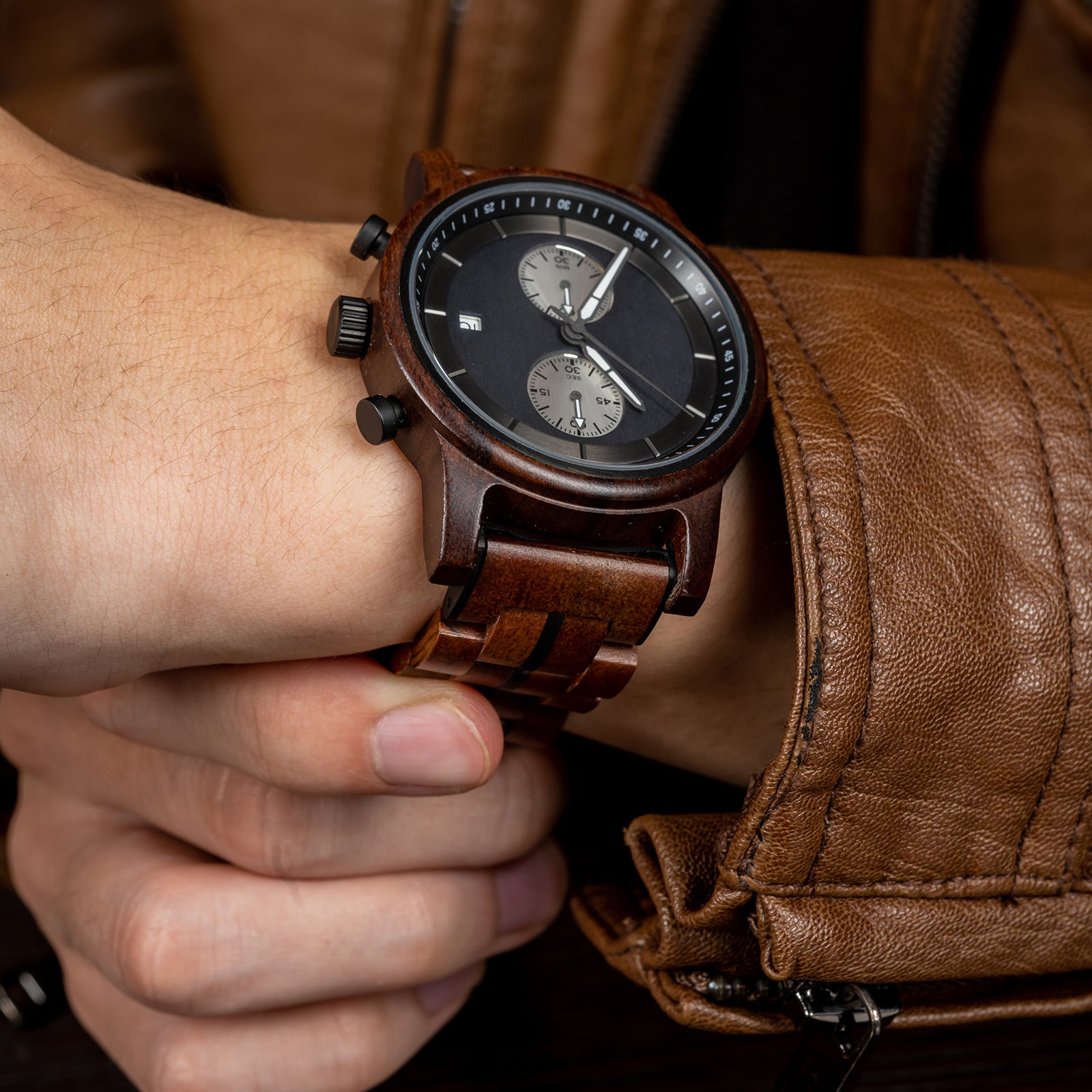 A stylish men's wooden chronograph watch with a dark gray dial, showcased on a wrist paired with a brown leather jacket, highlighting its sophisticated and rugged aesthetic in a lifestyle context.