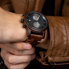 A stylish men's wooden chronograph watch with a dark gray dial, showcased on a wrist paired with a brown leather jacket, highlighting its sophisticated and rugged aesthetic in a lifestyle context.