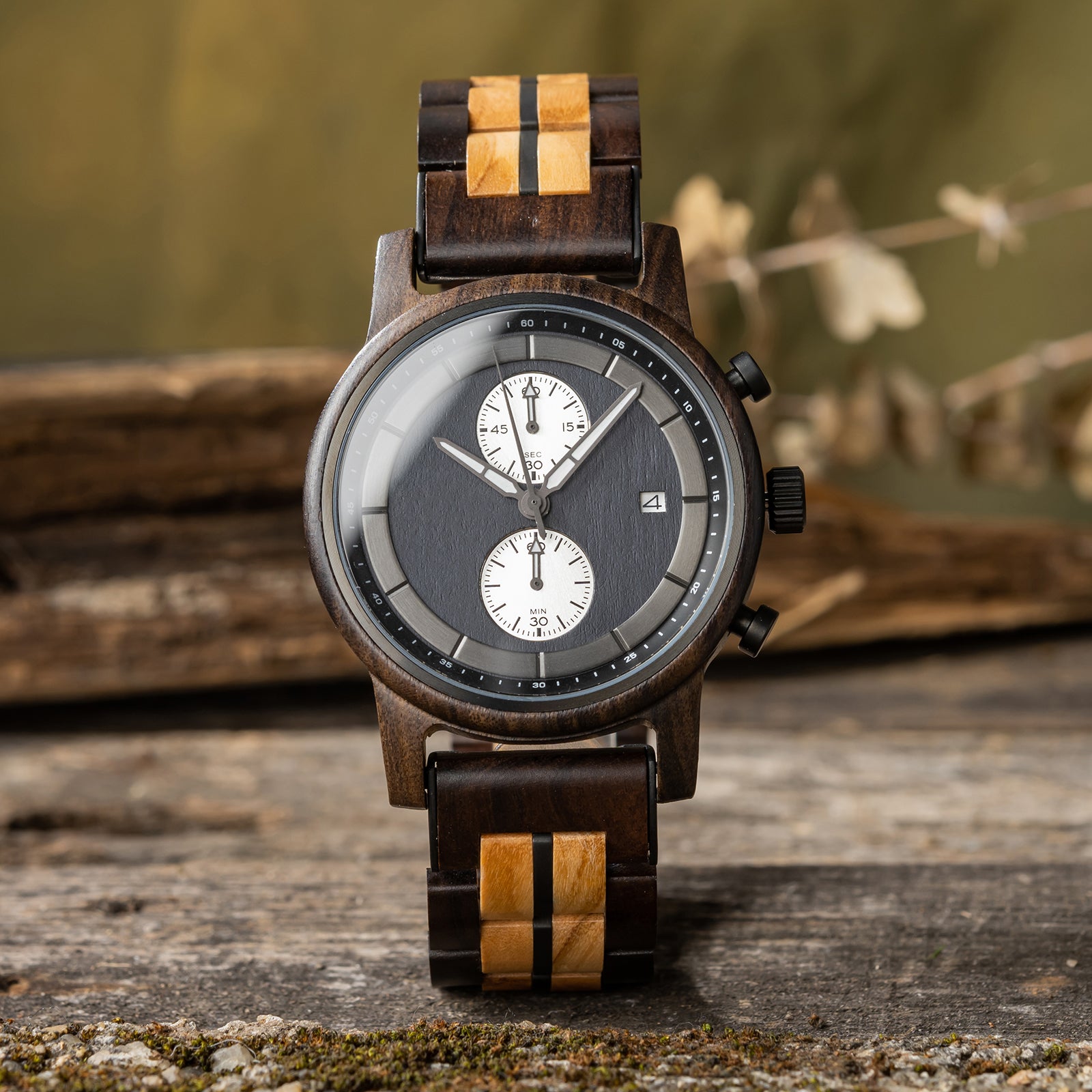 A stylish men's wooden chronograph watch featuring a two-tone wood band, dark gray dial, multiple sub-dials, and a date function, presented against a rustic wood background to highlight its sophisticated and natural aesthetic.