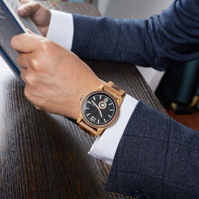A sophisticated men's wooden watch featuring a dark gray dial, showcased on a wrist wearing a navy suit while reading a book, highlighting its elegant and professional aesthetic.