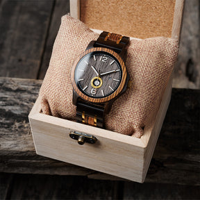 A sophisticated men's wooden watch featuring a dark gray dial, date and day display, natural wood grain band with gold accents, presented in a wooden box with a burlap pillow against a rustic wood background to emphasize its elegant and timeless packaging.