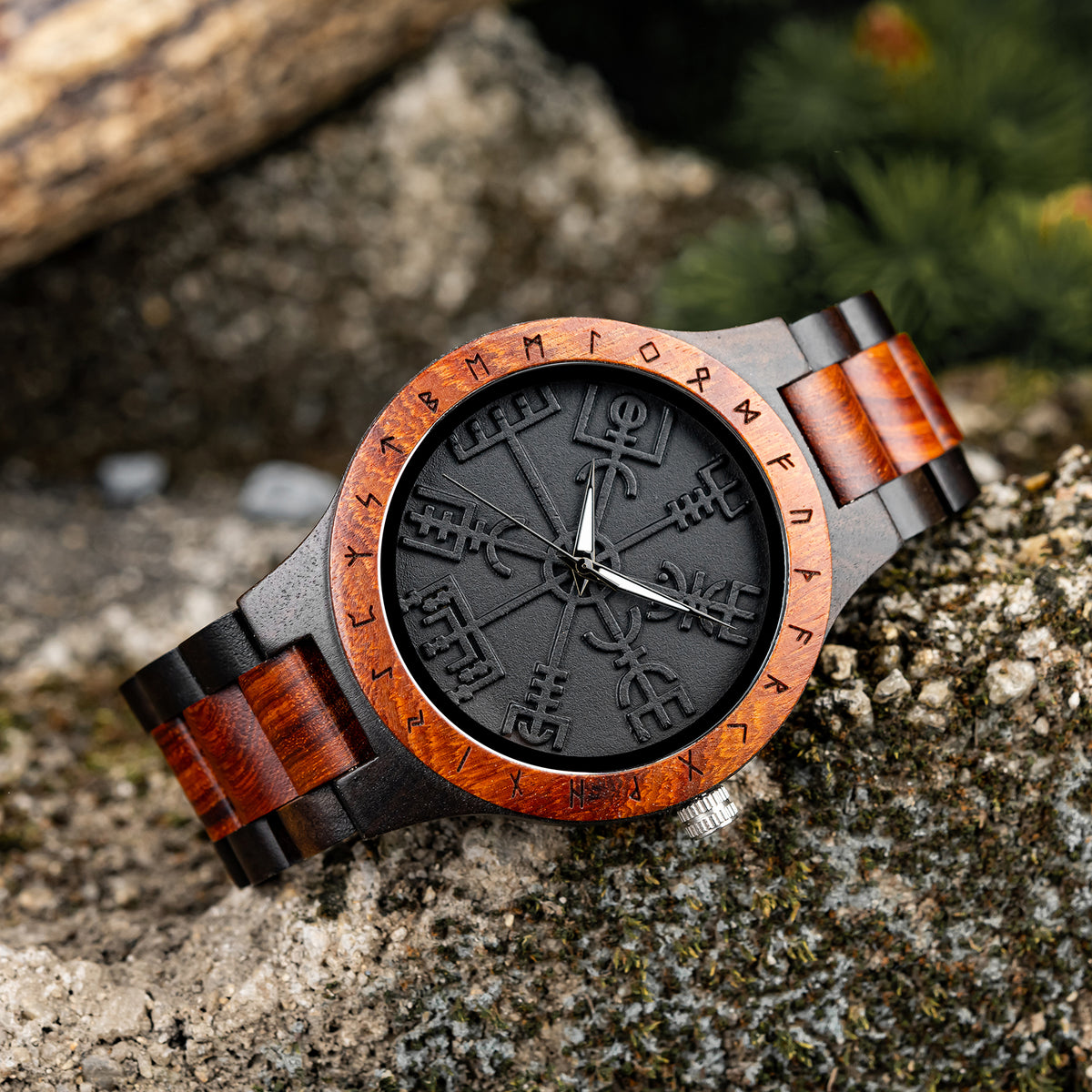 A unique men's wooden watch featuring a dial with Viking symbols, a bezel engraved with runes, and a two-tone wood band, presented on a rustic rock background to highlight its Norse-inspired and artisanal design.