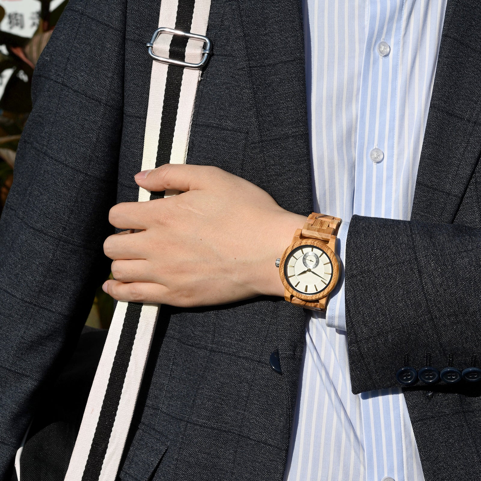 A sophisticated men's wooden watch featuring a white dial, sub-dial, textured light brown bezel, and gold-accented details, showcased on a wrist wearing a gray suit in an outdoor sophisticated setting, highlighting its refined and distinctive aesthetic.