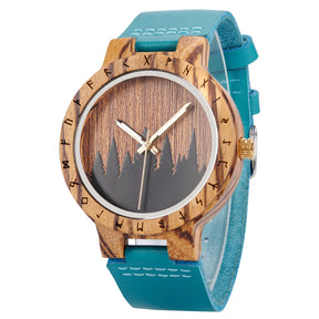 A distinctive wooden watch with a runic symbol bezel, forest silhouette dial, turquoise leather band, and gold-tone hands, showcasing a natural wood texture against a white background.