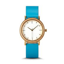 A minimalist women's watch featuring a wooden-accented bezel, white dial, gold-tone details, and a blue leather band, displayed against a white background.