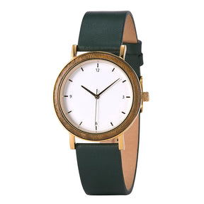 A minimalist women's watch with a wooden-accented bezel, white dial, gold-tone details, and a dark green leather band, presented against a white background.