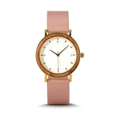 A minimalist women's watch featuring a wooden-accented bezel, white dial, gold-tone details, and a pink leather band, displayed against a white background.
