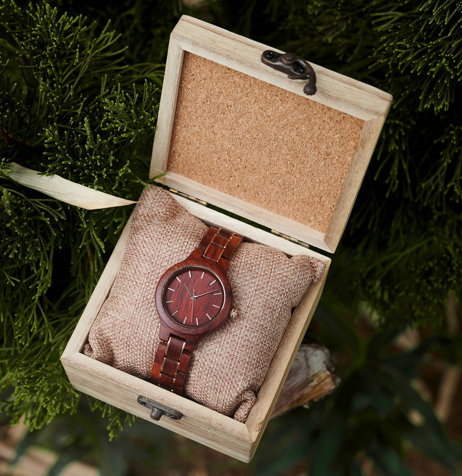 An elegant women's rosewood watch presented in a wooden box with a burlap cushion, set against a backdrop of lush greenery to emphasize its natural and refined packaging.