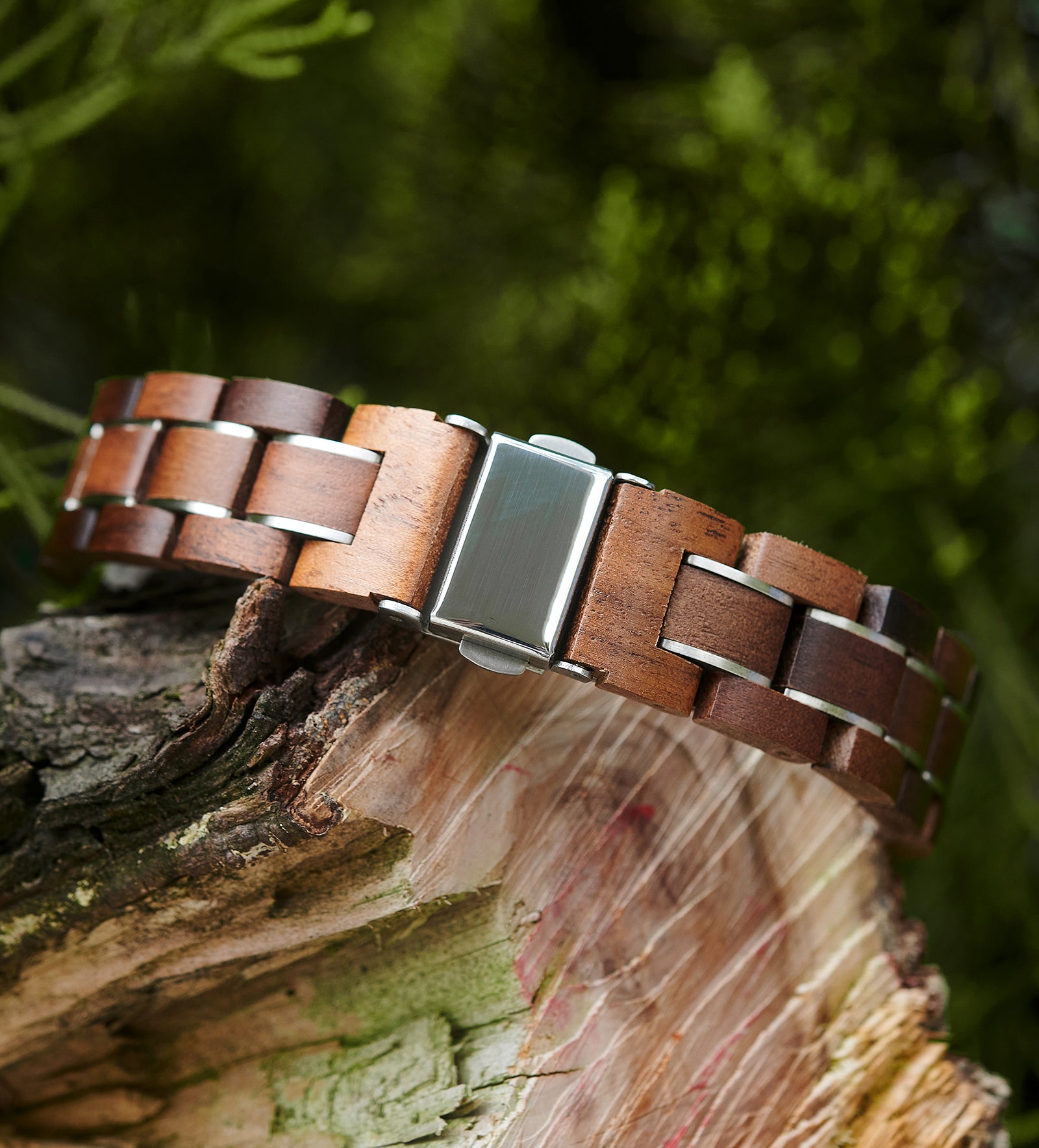 A detailed view of a women's walnut watch bracelet with a silver-tone clasp, displayed on natural wood amidst greenery to emphasize its craftsmanship and natural design.