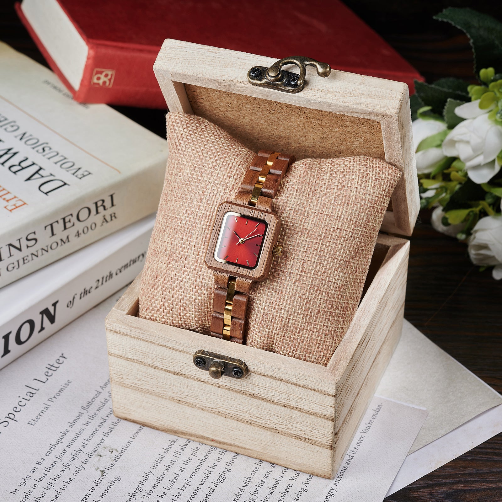 A sophisticated women's wooden watch with a red dial and gold accents, presented in a wooden box with a burlap cushion, set against a vintage background of books and flowers to emphasize its elegant and timeless packaging.