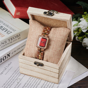 A sophisticated women's wooden watch with a red dial and gold accents, presented in a wooden box with a burlap cushion, set against a vintage background of books and flowers to emphasize its elegant and timeless packaging.