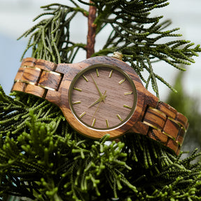A stylish women's zebrawood watch with gold-tone accents, displayed in detailed view amidst lush greenery to highlight its unique wood grain and elegant design.
