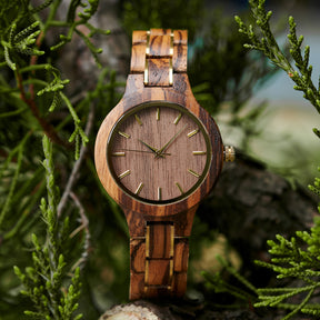 A stylish women's zebrawood watch with gold-tone accents, showcased amidst lush greenery to highlight its unique wood grain and elegant design.