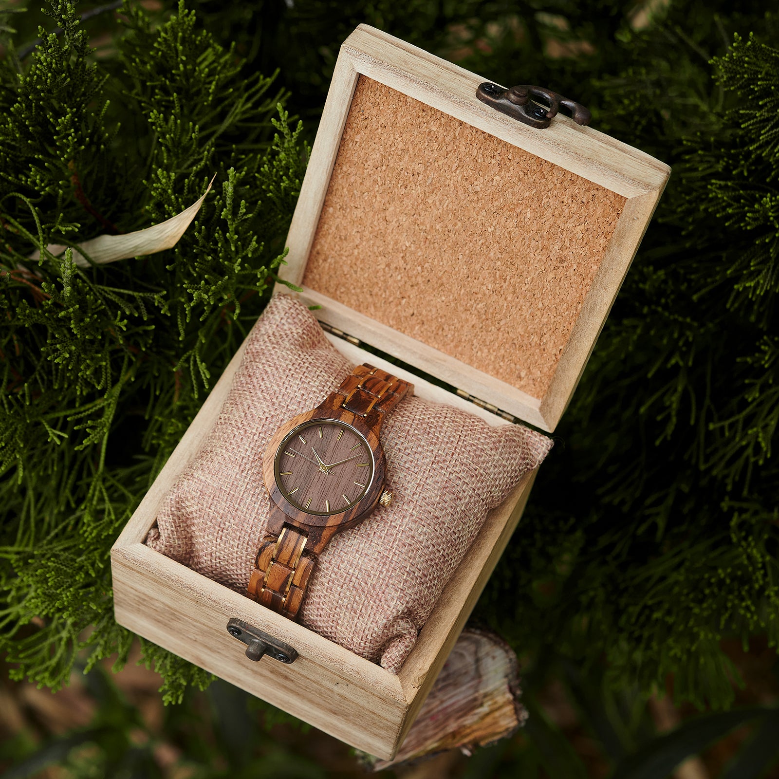 An elegant women's zebrawood watch presented in a wooden box with a burlap cushion, set against a backdrop of lush greenery to emphasize its natural and refined packaging.