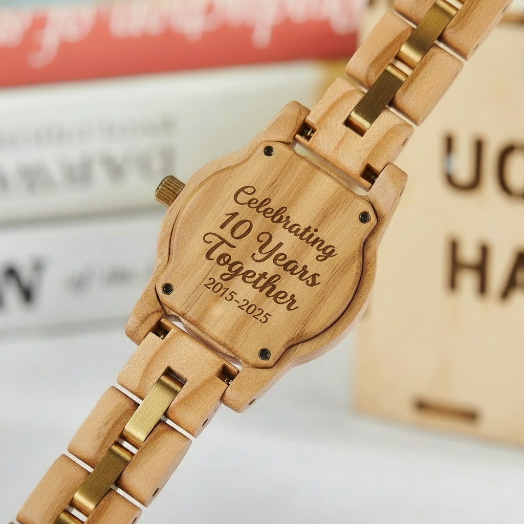 A detailed view of the back case of a women's wooden watch, showcasing its natural wood grain, gold-accented band, and structural design elements, set against a vintage book background.