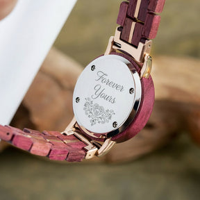 A detailed view of the back of a women's wooden watch, showcasing its red-purple wood band, gold accents, and metallic case back, highlighting the craftsmanship and design details.