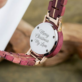 A detailed view of the back of a women's wooden watch, showcasing its red-purple wood band, rose gold accents, and metallic case back, highlighting the craftsmanship and design details.