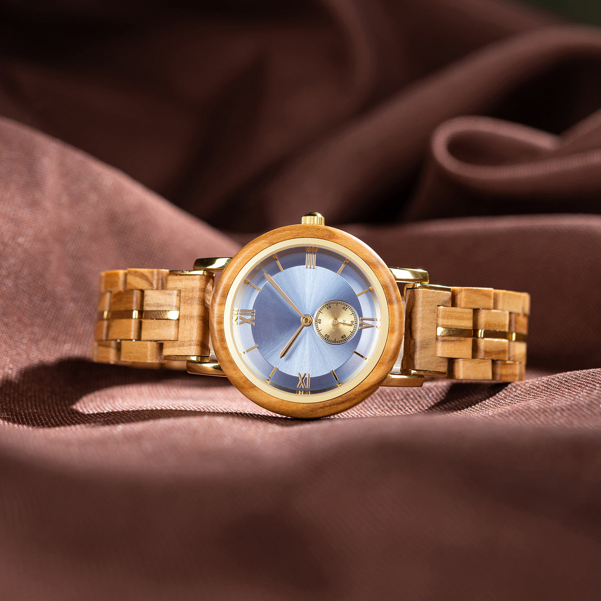 A stylish women's wooden watch featuring a blue dial, Roman numerals, sub-dial, and gold-accented details, presented against a brown fabric background to highlight its sophisticated and elegant aesthetic.